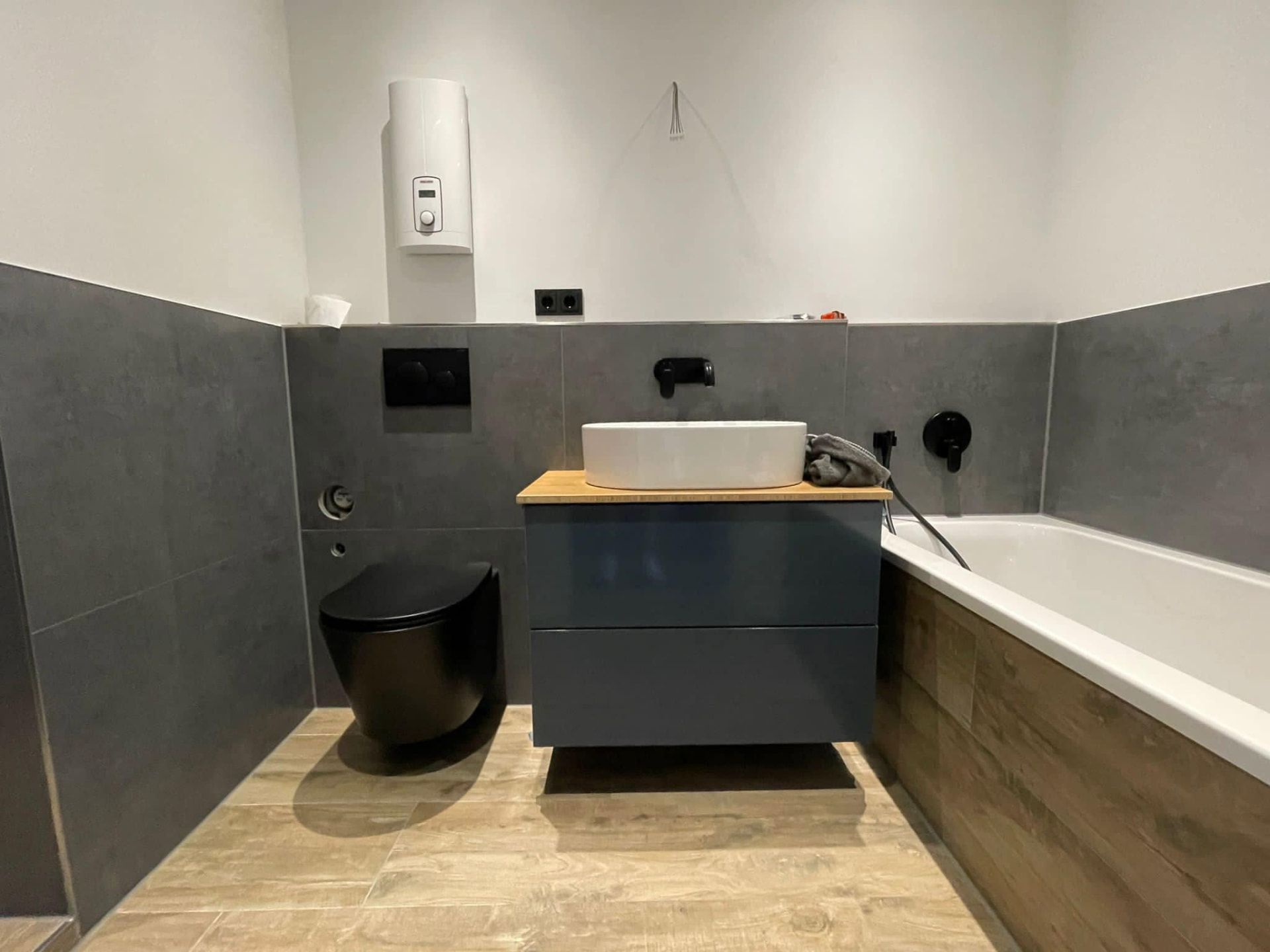 Waschtisch, schwarzes WC und Badewanne mit Holzoptik-Verkleidung